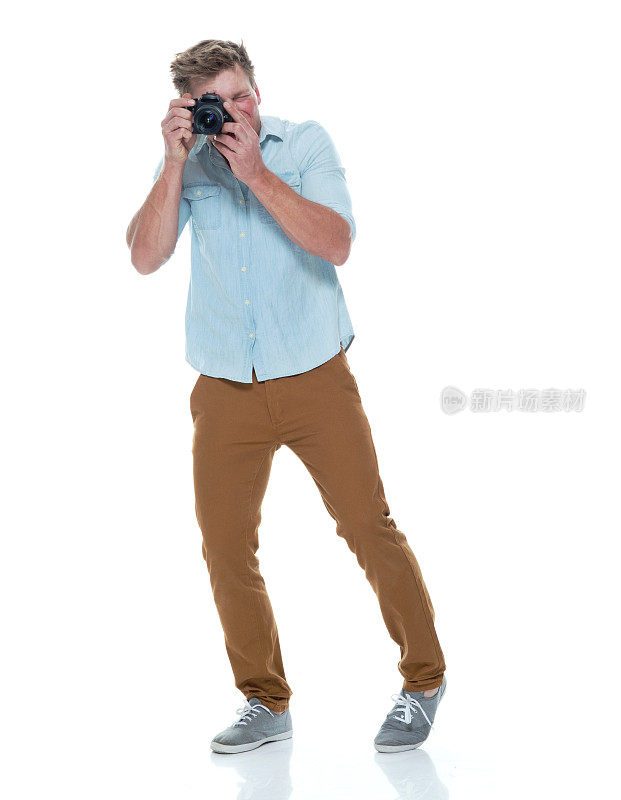一人/全身长度20-29岁英俊的人/短发白人男性/年轻男子摄影师/摄影在白色背景下穿着纽扣衬衫/裤子谁正在拍照/数码单反相机